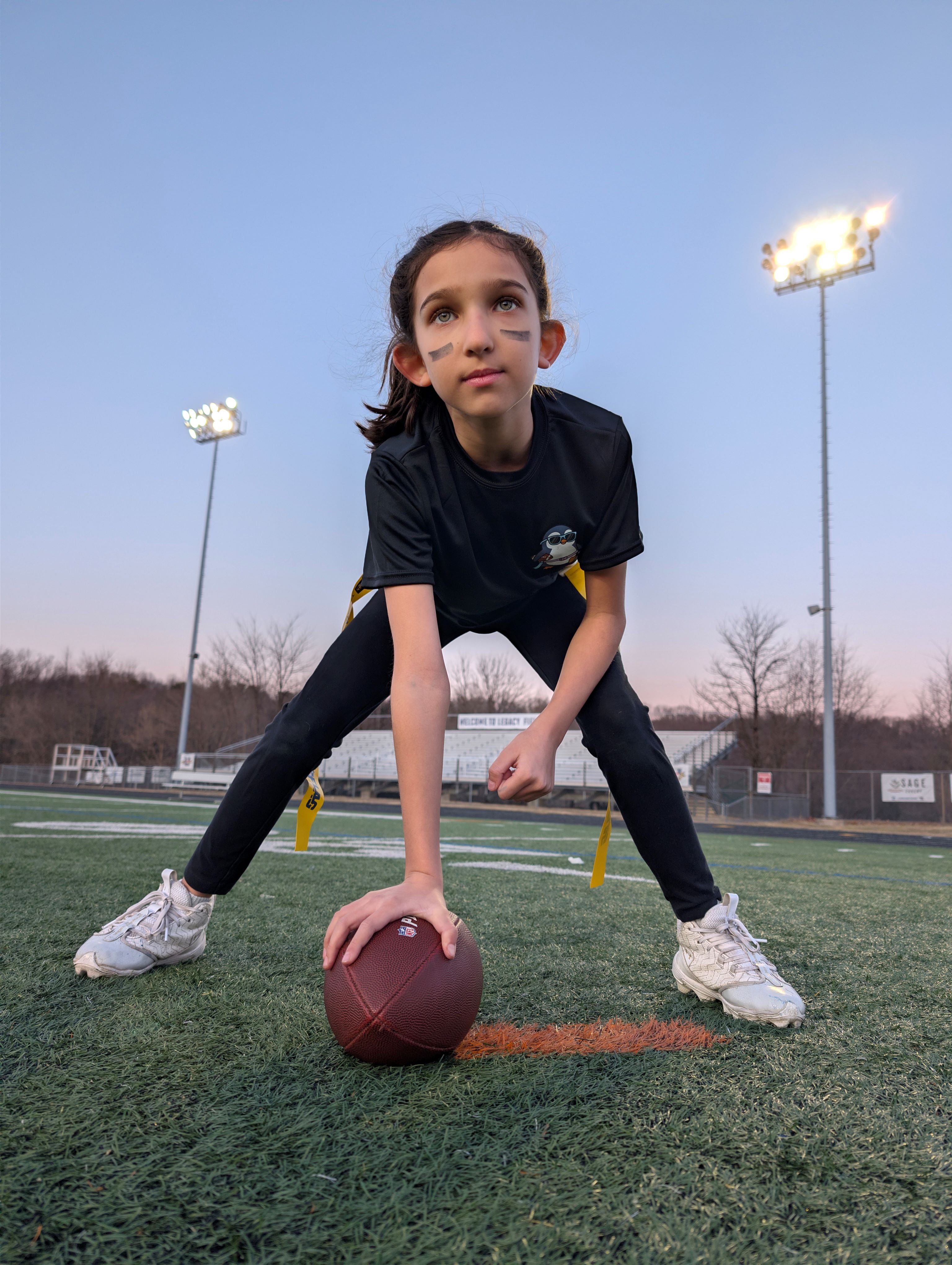 Young girl in football stance holding ball on field wearing Cool Beanz Flag Football apparel, youth flag football gear and performance clothing