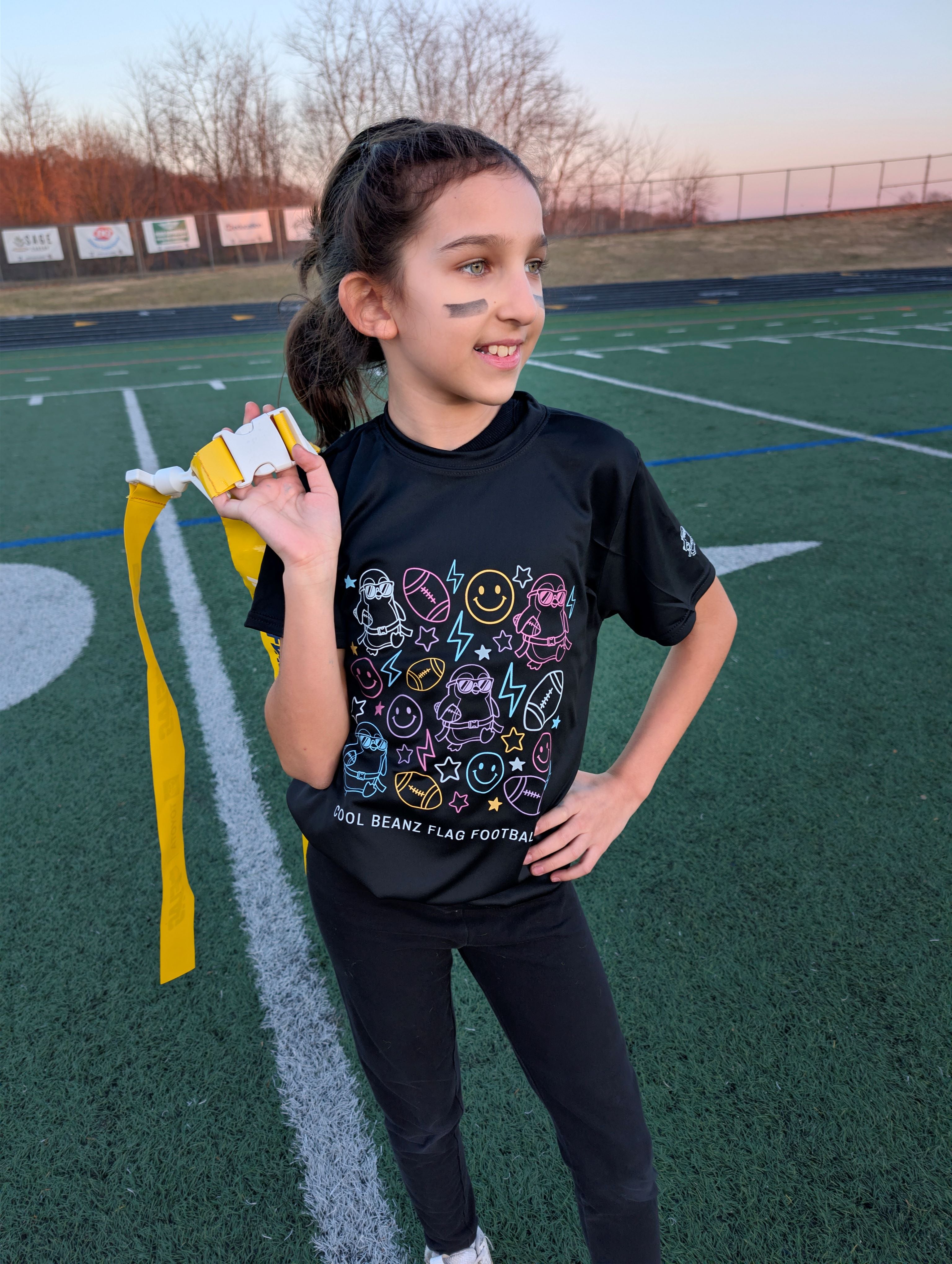 Girl wearing Cool Beanz Flag Football graphic t-shirt holding flag belt, stylish youth sports apparel for flag football players